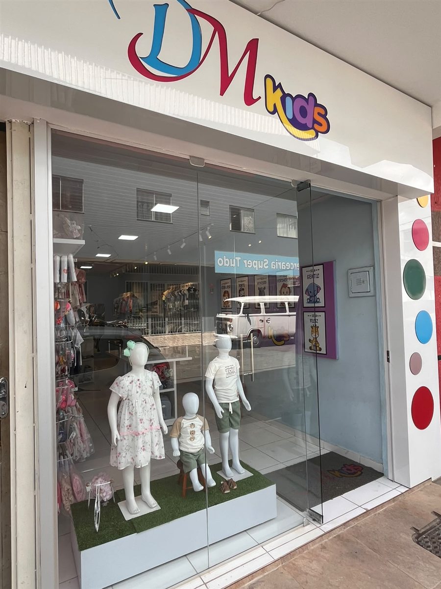 Fachada da loja DM Kids em Nova Serrana, com a logo na parede e manequins infantis na vitrine